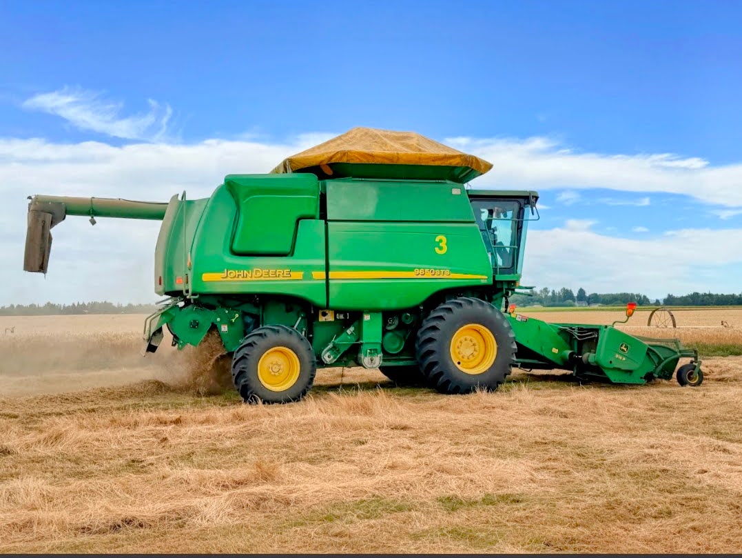Side view of a green John Deere 9650 STS combine harvesting a golden field, with dust trailing behind it.
